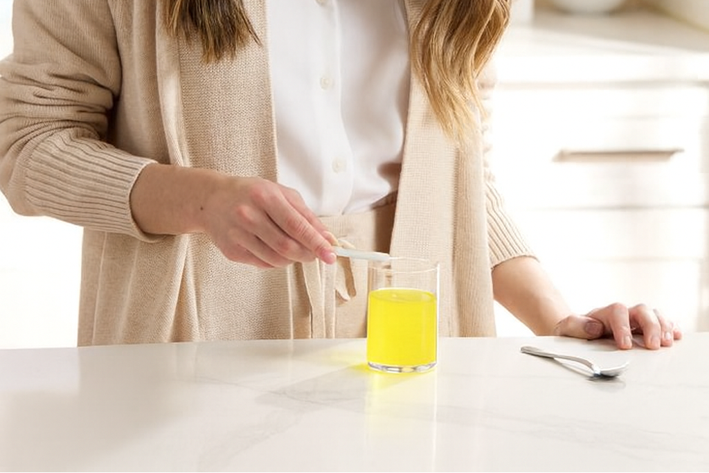 Woman in a kitchen preparing a drink with a glass of yellow liquid.